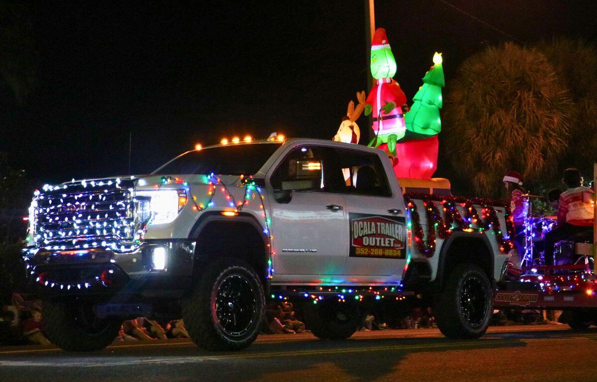 A truck with Christmas lights and a Grinch inflatable drives down a dark road.