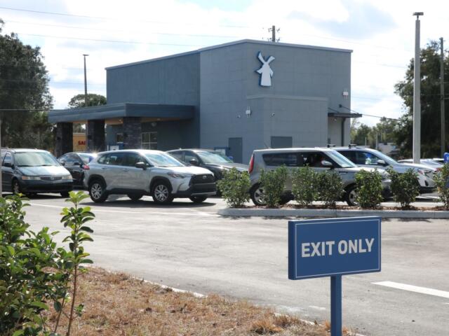 Cars lined up by a blue building with a drive-thru.