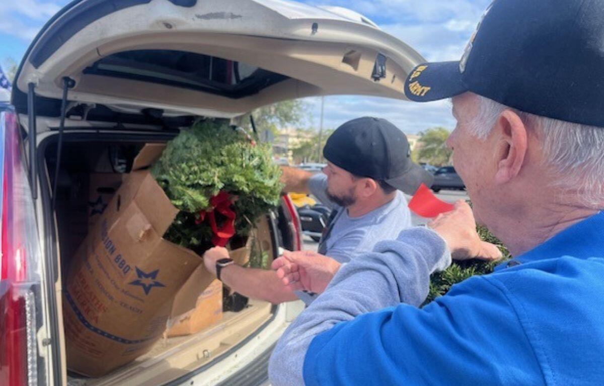 A man takes a pine wreath out of a box that's in an SUV.