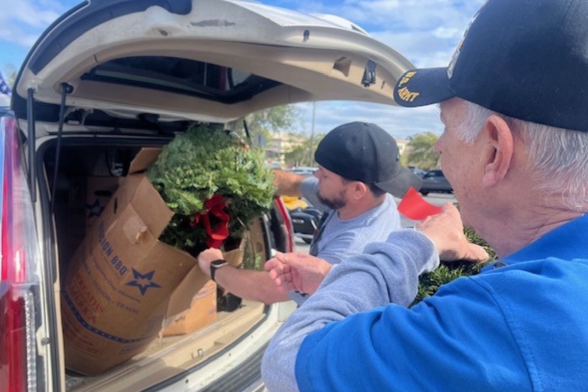 A man takes a pine wreath out of a box that's in an SUV.