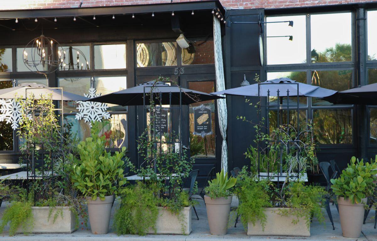 A restaurant front has vines and plants in planters with a black exterior and red bricks above the entrance.