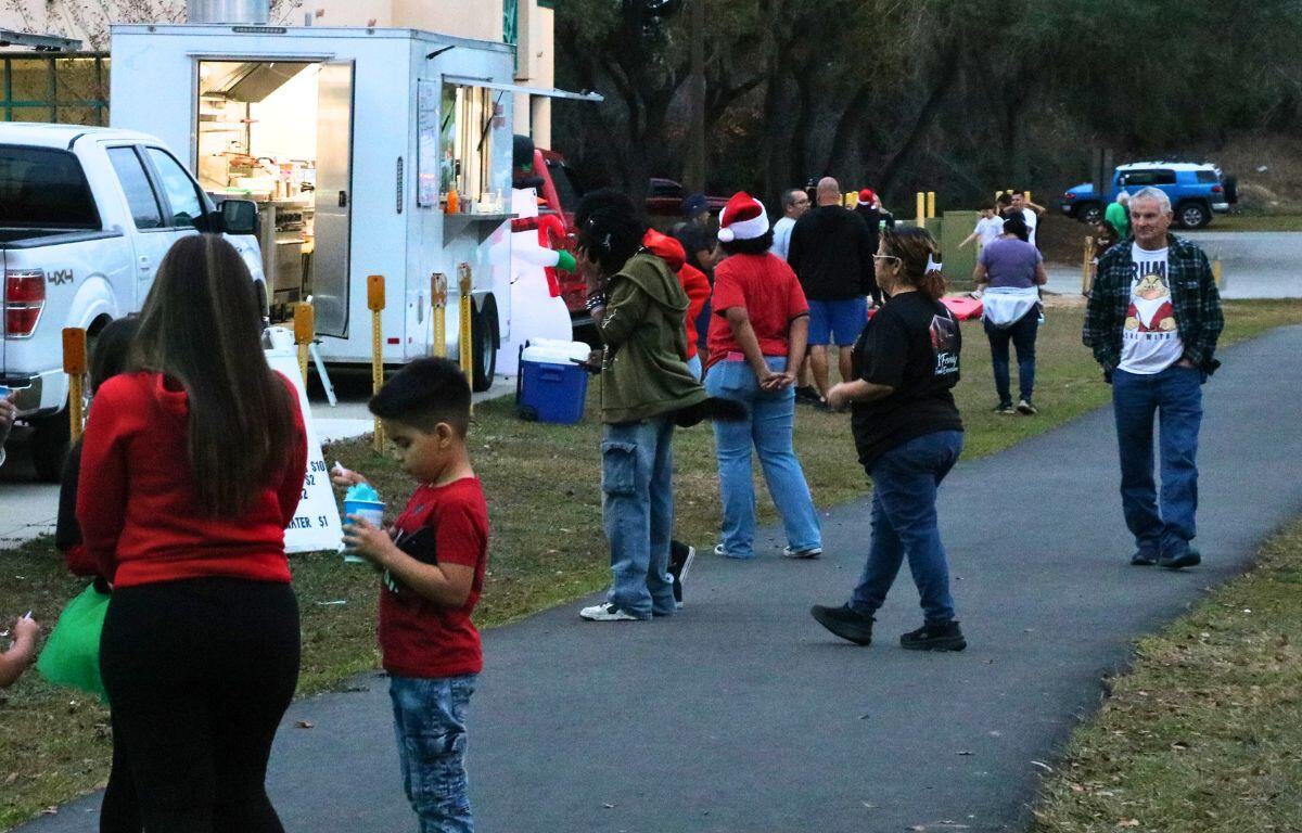 A crowd of people walk around food trucks and an open space on a paved pathway.