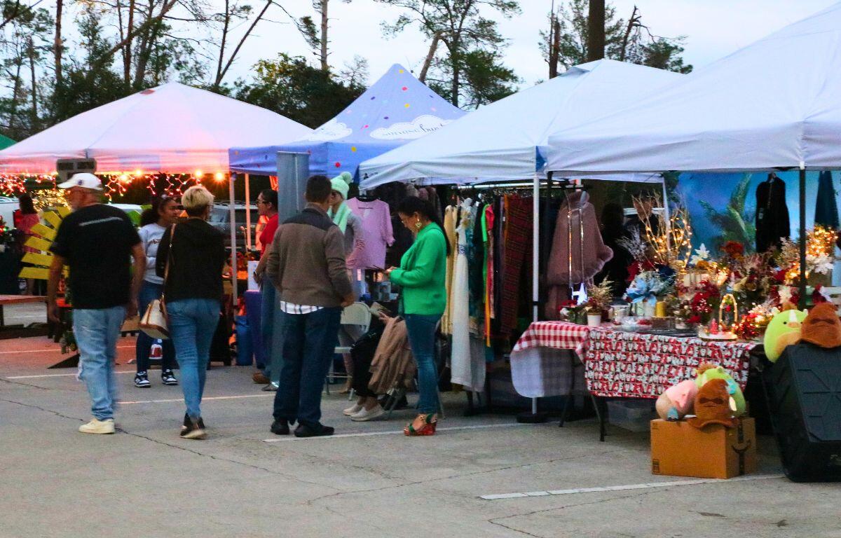 People walk along a parking lot taken over by vendor booths.