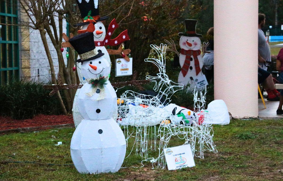 Snowmen, reindeer and more blow-up decorations sit in a grassy patch outside of a brick building.