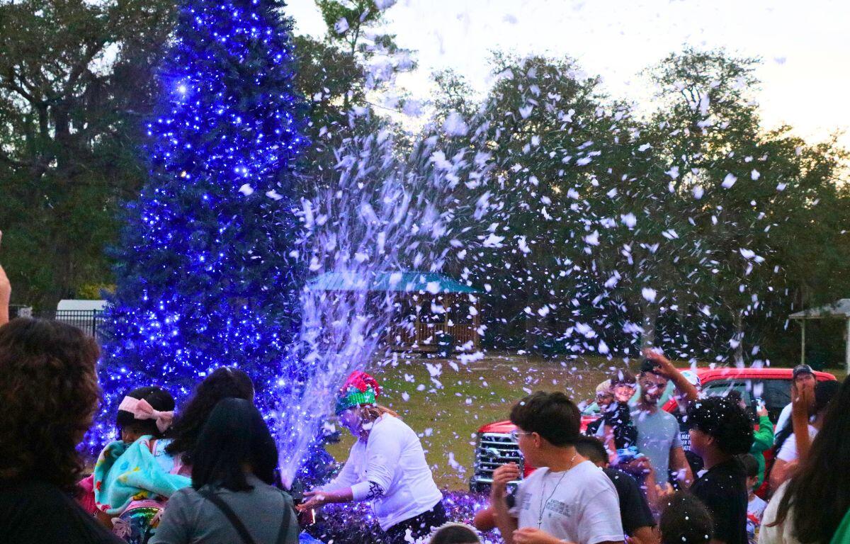 Fake snow foam shoots into a crowd of children as they catch and play in it.