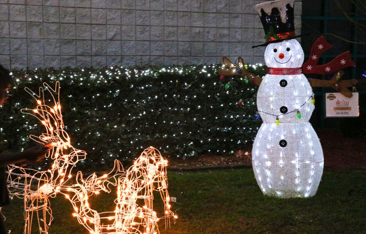 Reindeer and snowman decorations are brightly lit with bushes featuring string lights in the background.