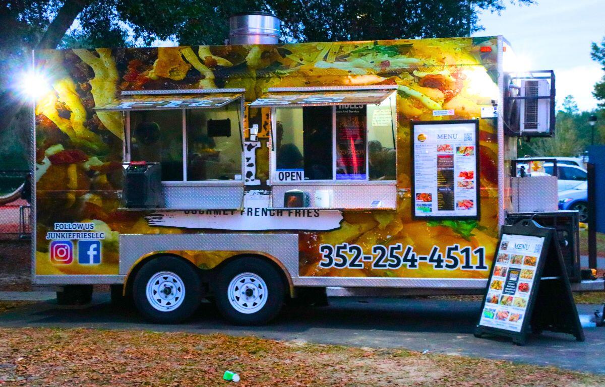 A food truck with a graphic of food covering it displays menus of their food option in a public park.