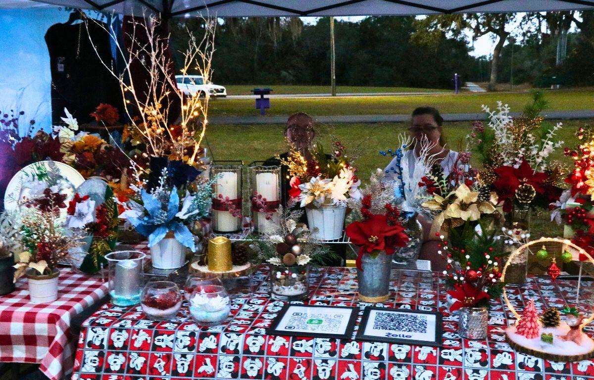 A vendor in a park features seasonal flowers with pay options displayed on the table.