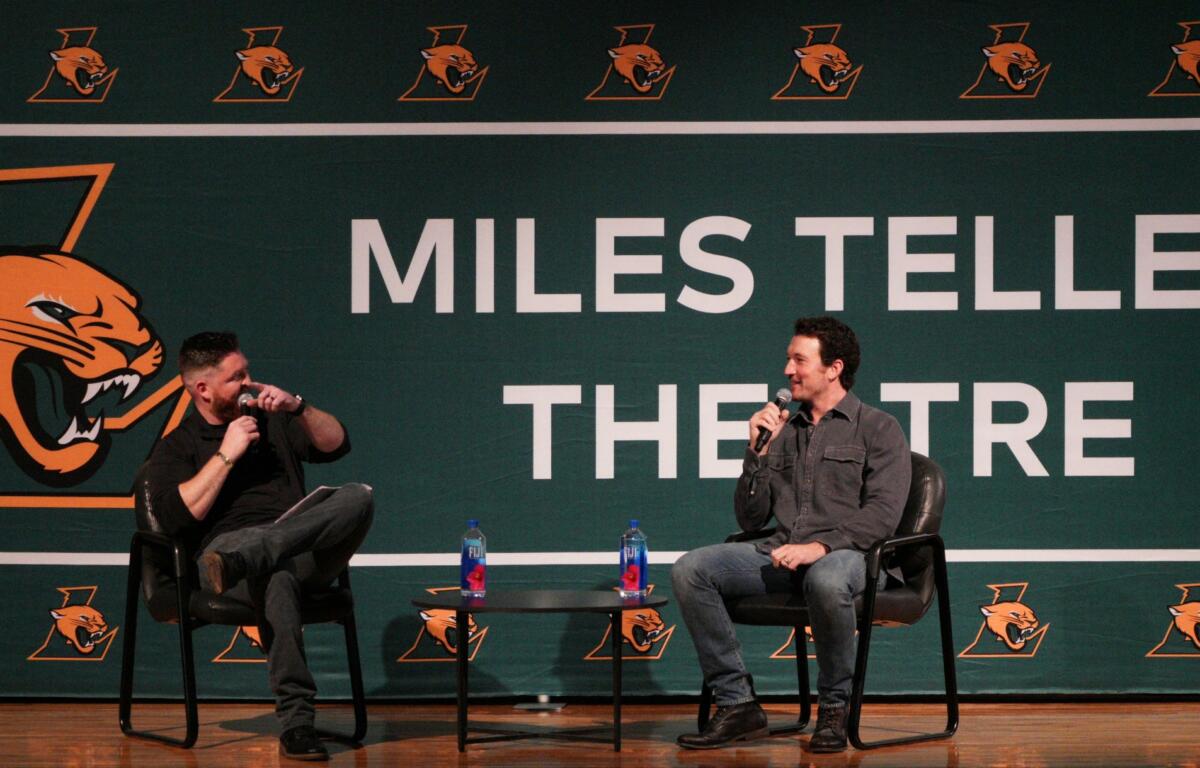 Miles Teller (right) and Ryan Downs (left) sit on black chairs in front of a sign that says "Miles Teller Theatre" for a Q&A session at a special assembly on Dec 5, 2025