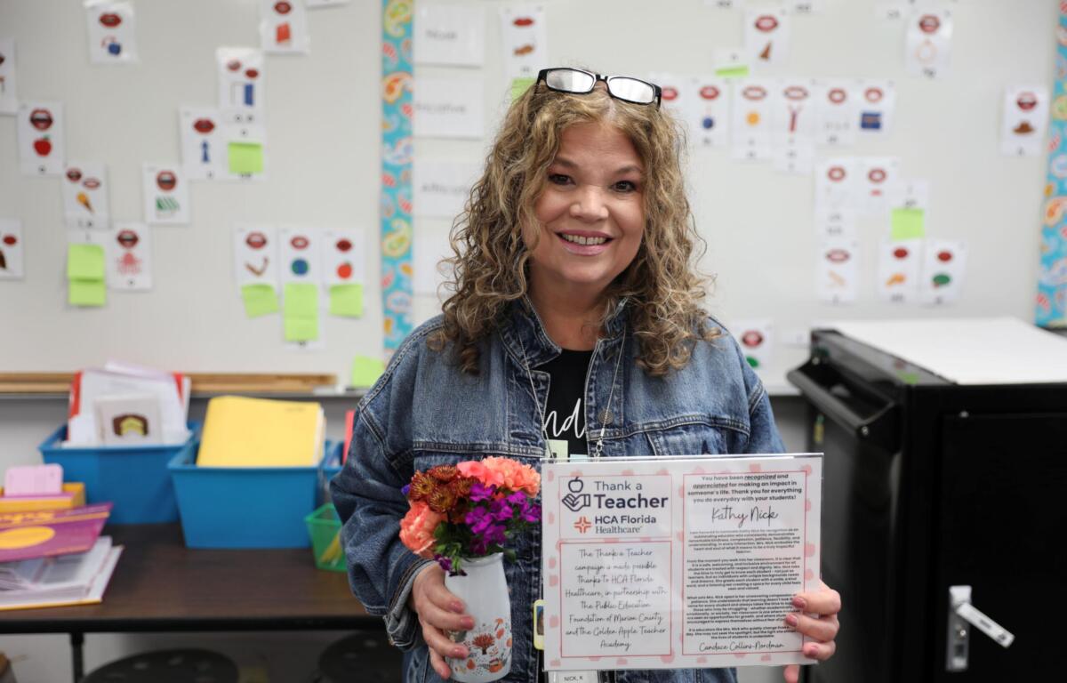 Kathy Nick, “Thank a Teacher” recipient stands with her certificate in one hand and a small vase with flowers in the other.