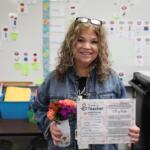 Kathy Nick, “Thank a Teacher” recipient stands with her certificate in one hand and a small vase with flowers in the other.