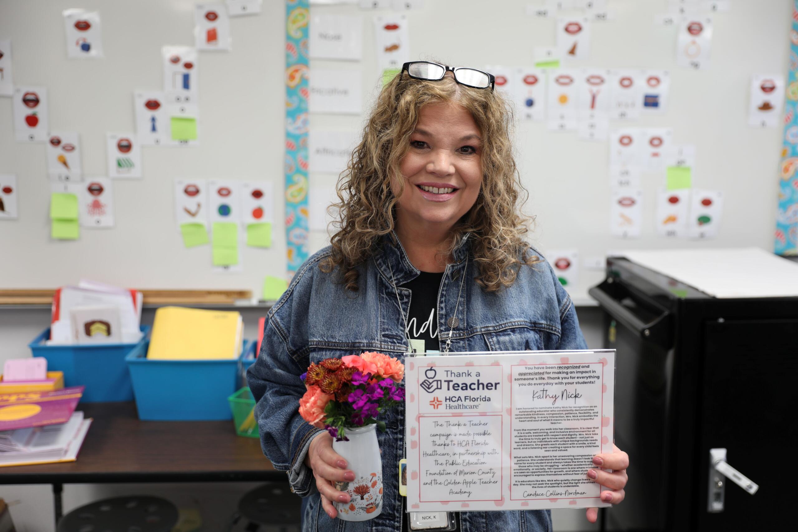 Kathy Nick, “Thank a Teacher” recipient stands with her certificate in one hand and a small vase with flowers in the other.