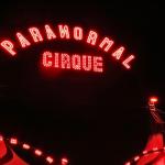 A neon sign reads, "Paranormal Cirque" above a red-lit black-and-white big top tent.