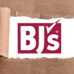 A red logo that reads, "BJs" with a checkmark as a apostrophe on a white backdrop with brown paper ripping up to reveal the logo and white background.
