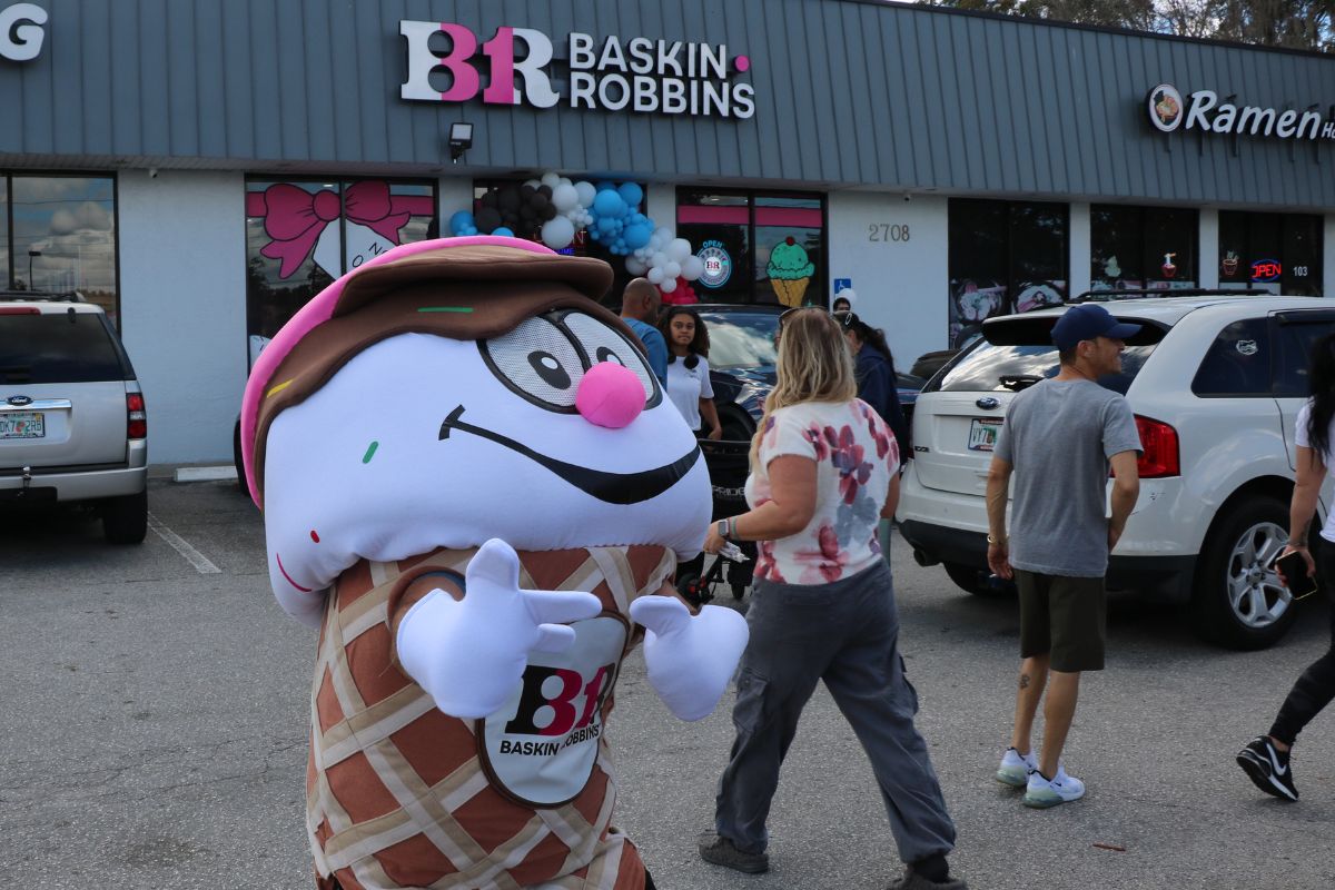 A person dressed as an ice cream cone in front of a Baskin Robbins, poses for a picture while advertising the new location.