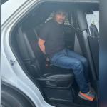 A man sitting in the back of a vehicle with his hands behind his back.