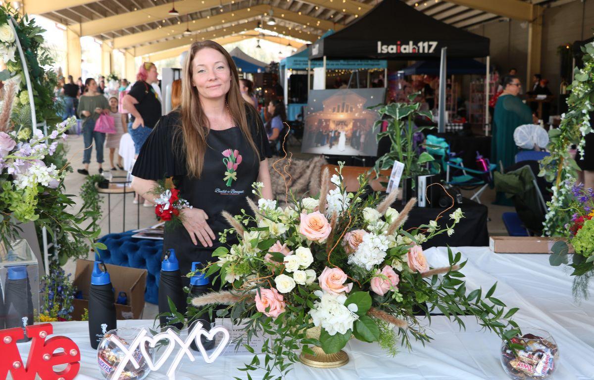 A woman stands behind a long table with a white tablecloth and bouquets of flowers.