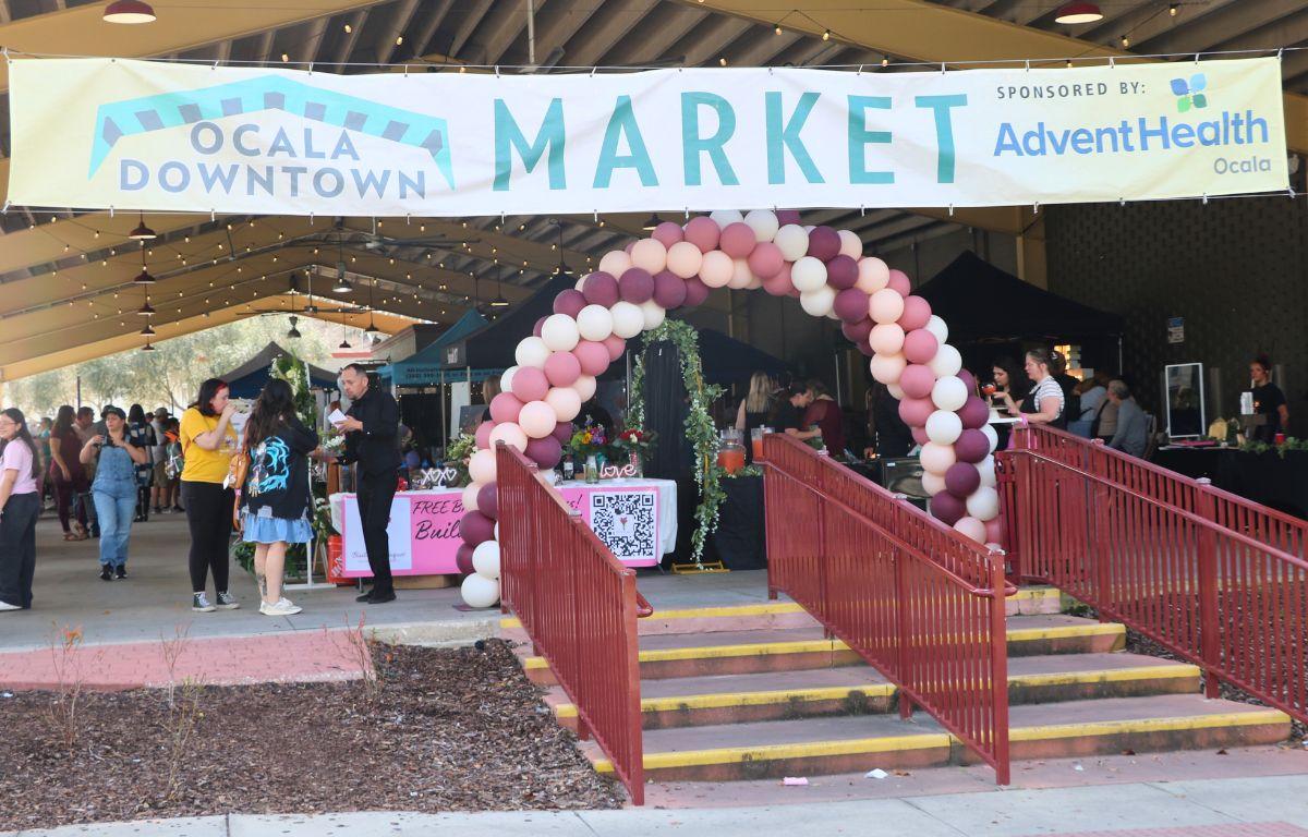 A large, open-air event area features a large balloon arch at the entrance with a white banner that reads, "Ocala Downtown Market. Sponsored by: Advent Health." A large market is taking place behind the entrance.