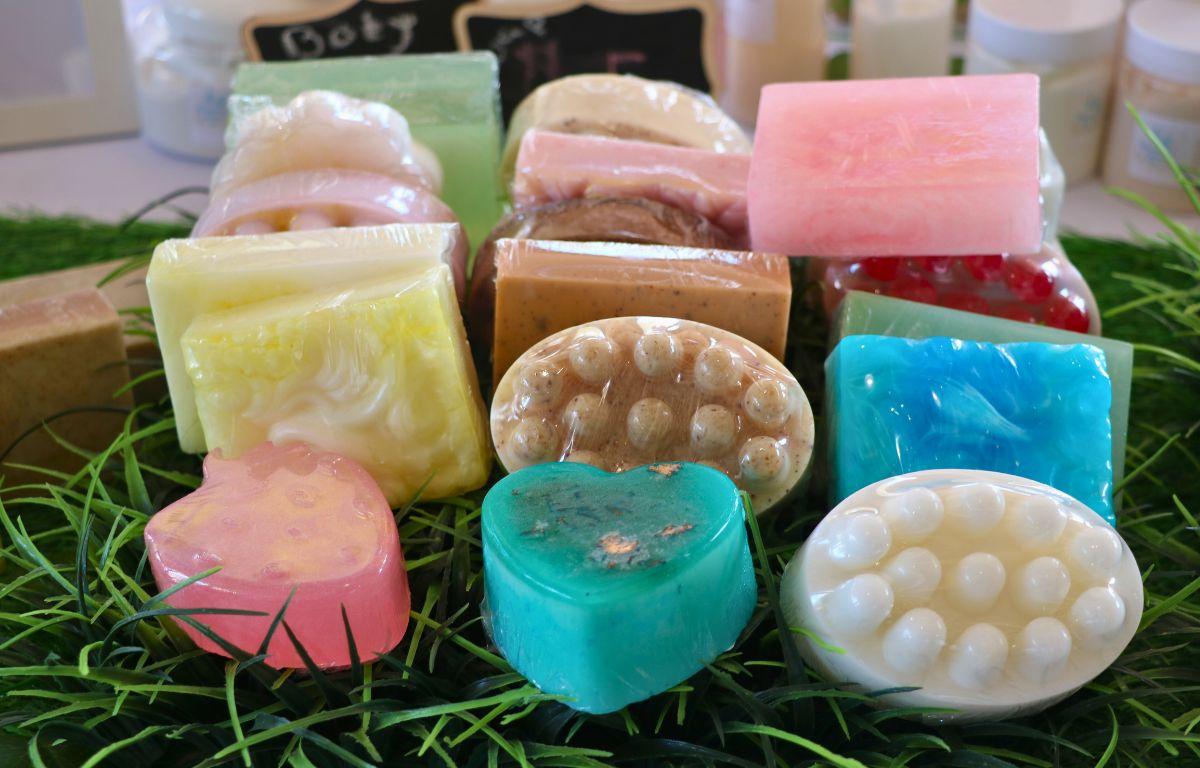 Handmade soaps in various colors and shapes sit on fake grass on a table.