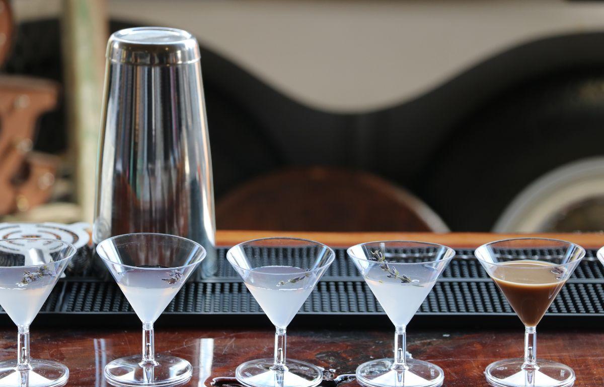 Martini glasses are filled with foggy and brown drinks with a silver shaker behind them on a bar stand.