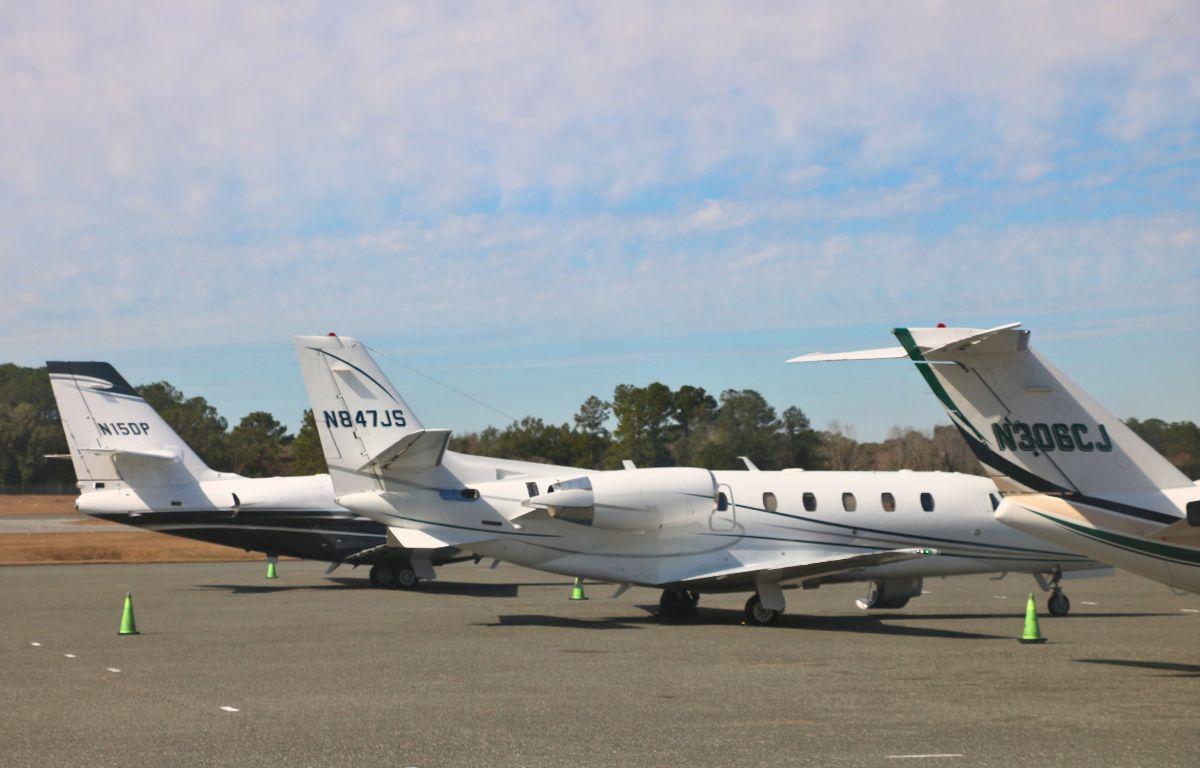 Large, white airplanes are lined up on a concrete strip. Green cones are scattered around them. The tail of the airplanes feature identification numbers.