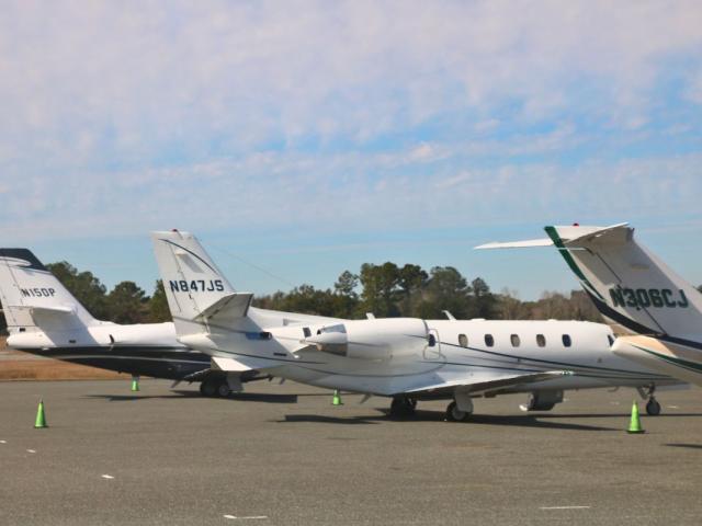 Large, white airplanes are lined up on a concrete strip. Green cones are scattered around them. The tail of the airplanes feature identification numbers.