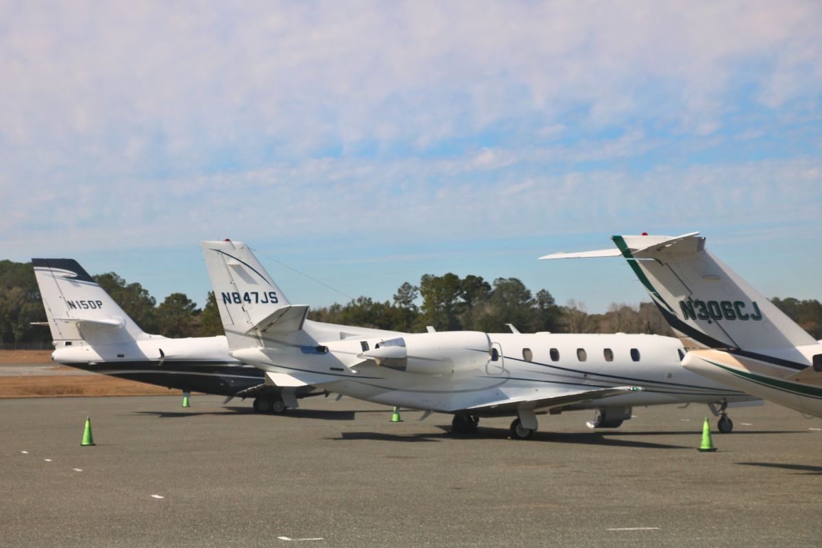 Large, white airplanes are lined up on a concrete strip. Green cones are scattered around them. The tail of the airplanes feature identification numbers.