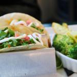 Two tacos sit on a taco holder with lettuce, tomato and sour cream on top. Next to the tacos is a small bowl of cooked vegetables.