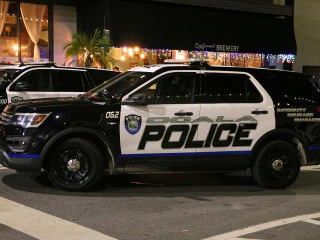 An Ocala police car sits in front of a line of shops at night. Lights hang from and overhang in front of Big Hammock's Brewery.