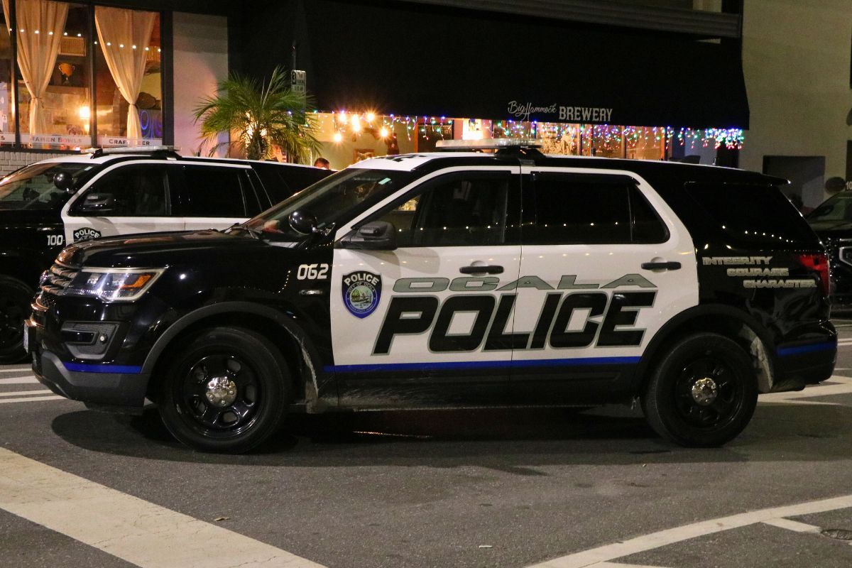 An Ocala police car sits in front of a line of shops at night. Lights hang from and overhang in front of Big Hammock's Brewery.