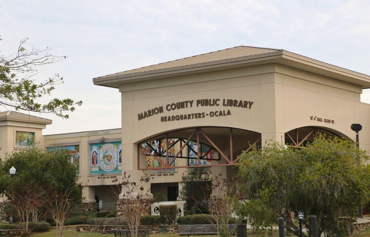 A library with an arched entrance and murals along its sides features a large letters above the arch reading, "Marion County Public Library Headquarters - Ocala."