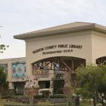 A library with an arched entrance and murals along its sides features a large letters above the arch reading, "Marion County Public Library Headquarters - Ocala."