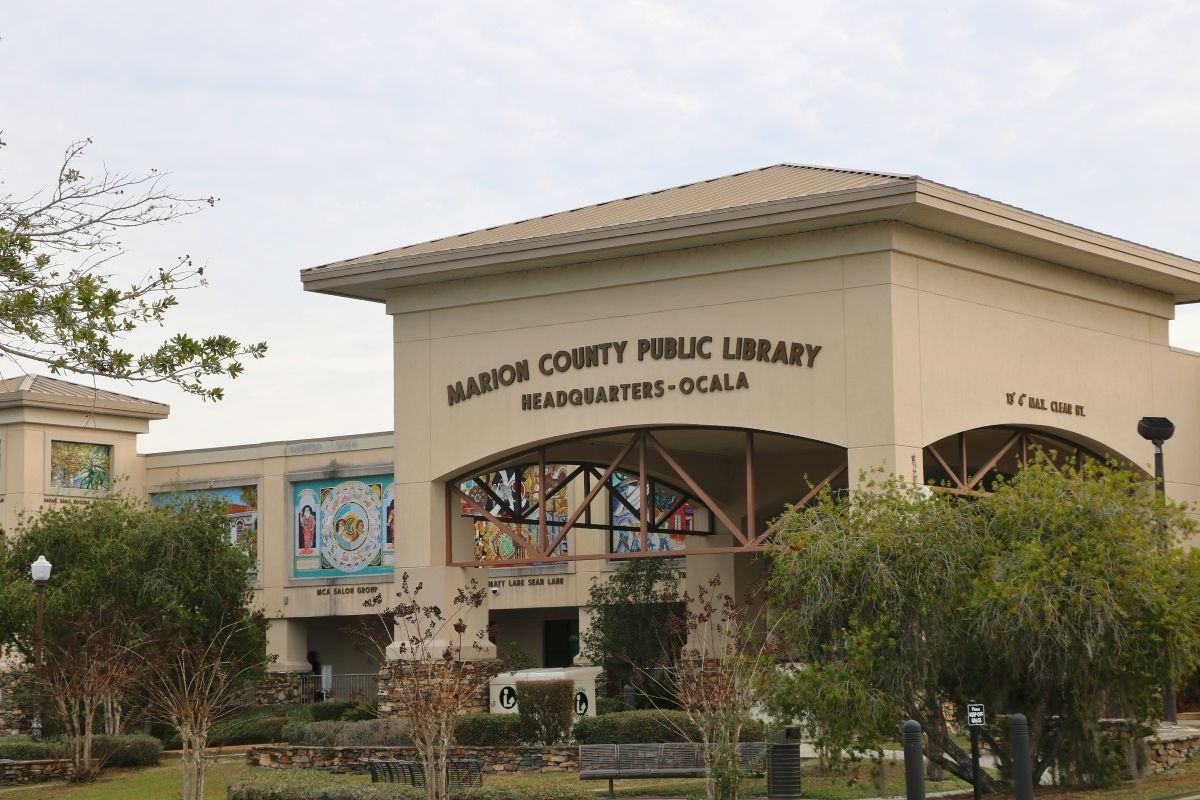 A library with an arched entrance and murals along its sides features a large letters above the arch reading, "Marion County Public Library Headquarters - Ocala."