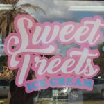 A pink, white and blue sign on a glass window reads, "Sweet Treets Ice Cream."