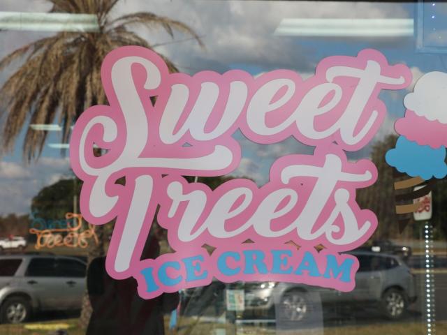 A pink, white and blue sign on a glass window reads, "Sweet Treets Ice Cream."