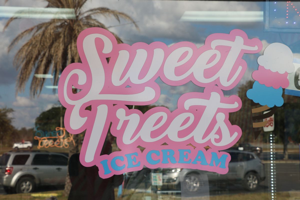 A pink, white and blue sign on a glass window reads, "Sweet Treets Ice Cream."