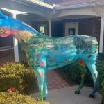 Shrubbery on the left, a fiberglass horse in the foreground on a concrete platform, trim and columns in the background, and in the far background, brick, windows and doors.