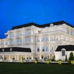 A large building stands in a grass field with a dark blue sky in the background and lights shinning on the building in the area.