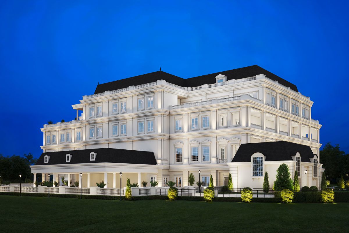 A large building stands in a grass field with a dark blue sky in the background and lights shinning on the building in the area.