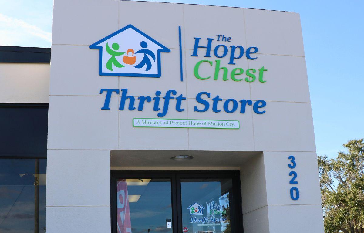 A storefront features a white wall with glass doors. Blue and green letters read, "The Hope Chest Thrift Store. A Ministry of Project Hope of Marionn Cty."