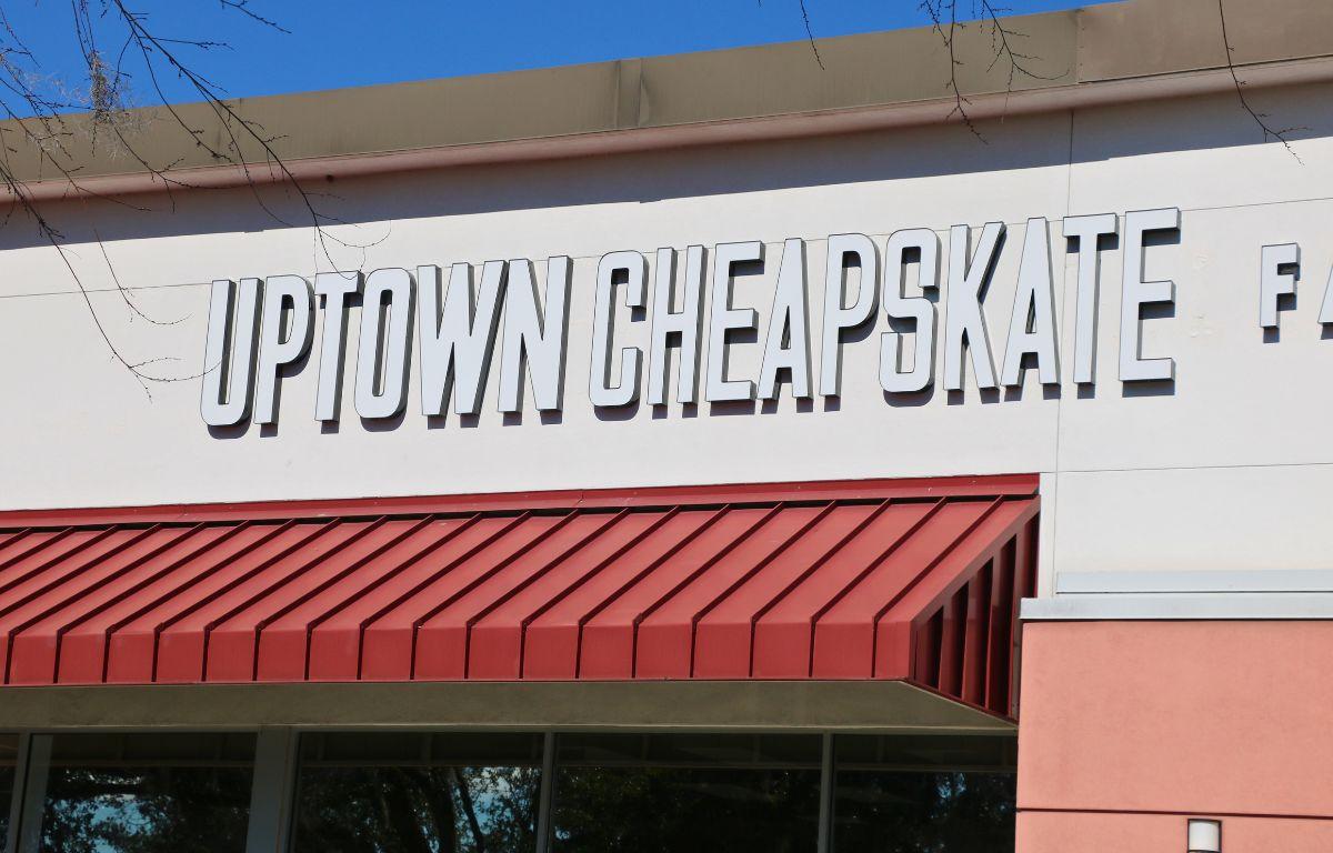 A closeup of a white building with red overhangs features a large, white sign reading, "Uptown Cheapskate."