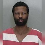 A man in an orange and white jump suit standing against a gray wall.