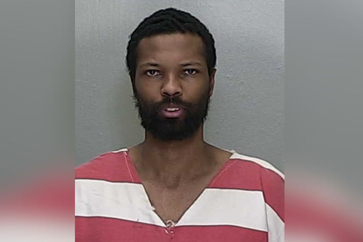 A man in an orange and white jump suit standing against a gray wall.