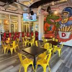 A colorful dining space with yellow metal chairs and wooden tables. A mural of an alligator in a Florida Gators jersey posing with a football player sits in the background.