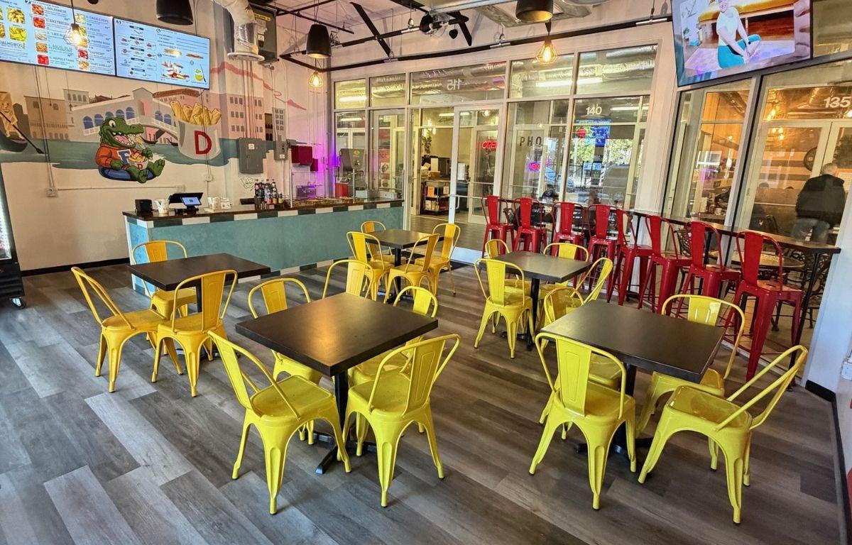 A colorful dining space with yellow metal chairs and wooden tables. A mural in the background.