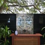 The entrance of a restaurant features a wooden hostess stand in front of a metal panel with text that reads, "Bank Street." The panel is against a black, wooden wall with plants on either side of the hostess stand.