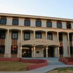 A large, brick building features stairs line with yellow metal railings and short, red brick walls. Over the entrance is a smaller overhang with red letters on the front reading, "city hall."