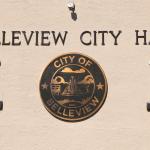 A beige building features a large City of Belleview logo with small windows on either side of it. above the logo is letters reading, "Belleview City Hall." Above the letters is a small camera.