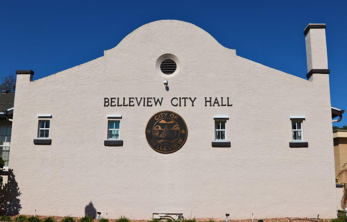 An old building features windows lining a wall with a large, City of Belleview logo in the center and letters above it reading, "Belleview City Hall."