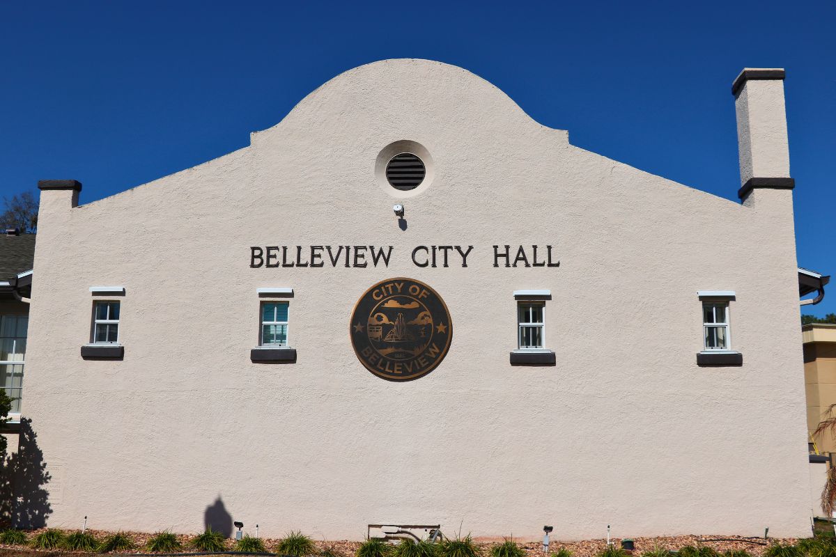 An old building features windows lining a wall with a large, City of Belleview logo in the center and letters above it reading, "Belleview City Hall."